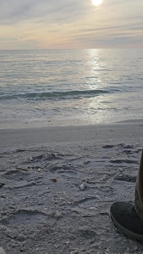 Sandy beach with ocean waves rolling in at sunset with person's foot Video stock 301900750