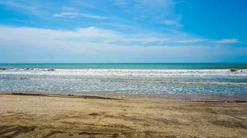 Sandy Beach With Ocean Waves Under a Blue and White Sky Stock Photos
