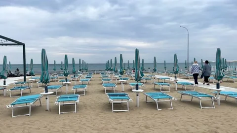 Sandy beach with parasols and empty deck chairs awaiting tourists. Holiday hotel Stock Footage 213841682