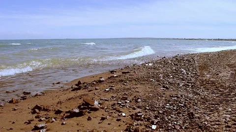 Sandy beach with rocks, waves, wind and blue sky. Stock Footage
