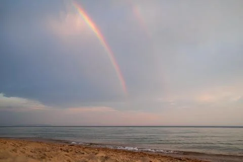 A sandy beach with shells and a turquoise sea against a rainbow sky backgroun Foto stock