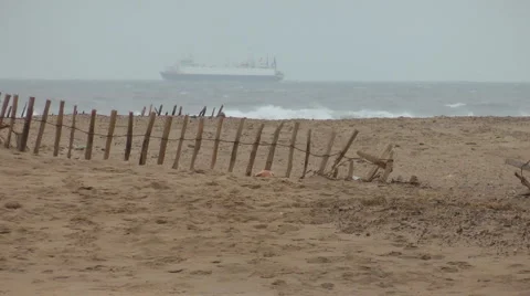 Sandy beach with storm battered wood and wire fence, cargo ship on horizon Stock Footage 1092015