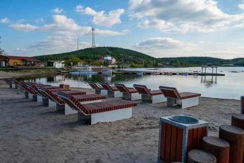 Sandy beach with sun beds on the background of a pier, boats and mountains Stock Photos