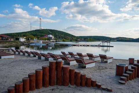 Sandy beach with sun beds on the background of a pier, boats and mountains Stock Photos
