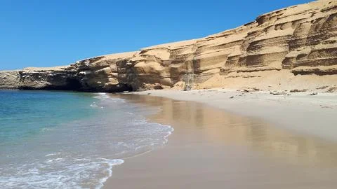 Sandy beach with turquoise waves lapping the shore beneath towering golden Stock Photos