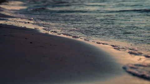 The sandy beach is washed by sea waves with foam in the rays of the setting sun Stock Footage 243976311