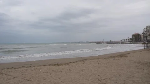 Sandy Beach with Waves and Coastal Buildings Under Overcast Sky 库存影片 333618119