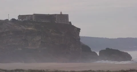 Sandy beach with waves breaking and rocky cliff with castle and lighthouse Stock Footage 155604966