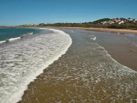 Sandy beach with white ocean waves and blue sky. Stock Photos