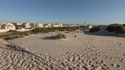 Sandy dunes with patches of grass lead toward coastal buildings Stock Footage 346290538