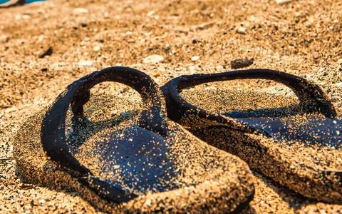 Sandy Flip Flops Resting on a Beach with Ocean Waves in the Background Stock Photos