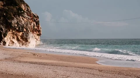 Sandy foreground, dramatic rocky cliff on the left and turquoise waves Stock Footage 328932941