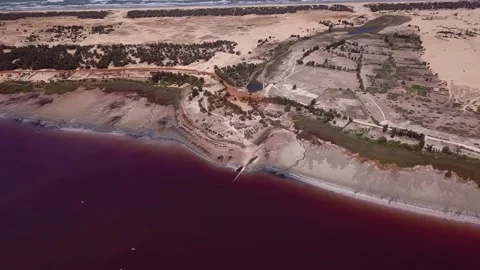 Sandy land with trees between dark pink lake and ocean with waves crashing Stock Footage 208937249