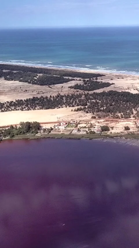 Sandy land with trees between dark pink lake and ocean with waves crashing 스톡 동영상 230675192