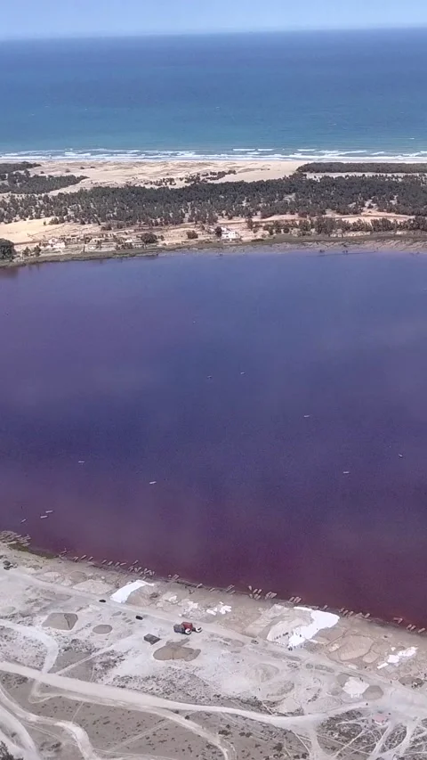 Sandy land with trees between dark pink lake and ocean with waves crashing Video stock 230675794