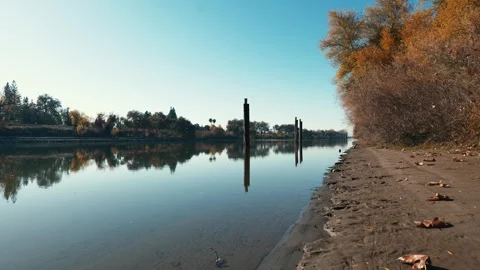 Sandy levee on river with pillars sticking out of water and reflections Stock Footage 259216013