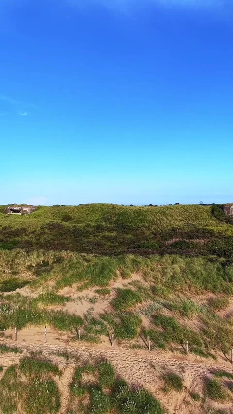 A sandy path winding among grass-covered dunes toward a wooden fence. Stock Footage 337349642