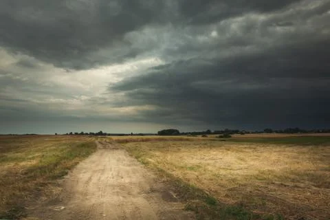 Sandy road through fields and dark stormy clouds Stock Photos