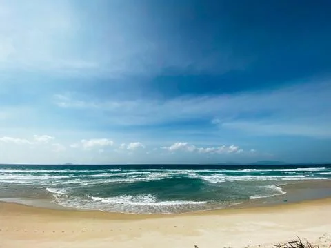 Sandy seashore, calm soft waves at sea, sunny weather, blue sky with white cl Stock Photos