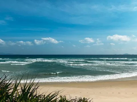 Sandy seashore, calm soft waves at sea, sunny weather, blue sky with white cl Stock Photos