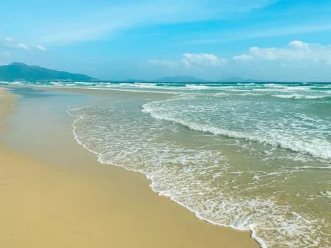 Sandy seashore, calm soft waves at sea, sunny weather, blue sky, white clouds Stock Photos