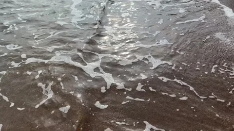 Sandy shoreline with gentle waves rolling in, creating white foam and wet san Stock Footage 321764294
