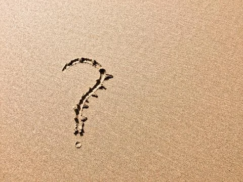 A sandy surface bears a clear question mark, indicating a query or doubt. Stock Photos