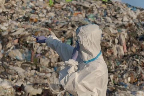 A sanitation worker in protective gear points at a towering mountain of tra.. Stock Photos