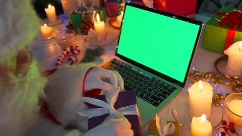 Santa with beard adjusts bow on present box at computer with chromakey screen Stock Footage 255850471