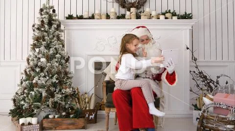 Santa Claus and cute little girl taking Christmas selfies on tablet Stock Photos
