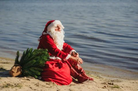 Santa Claus on the beach drinks whiskey and smokes a cigar. Stock Photos