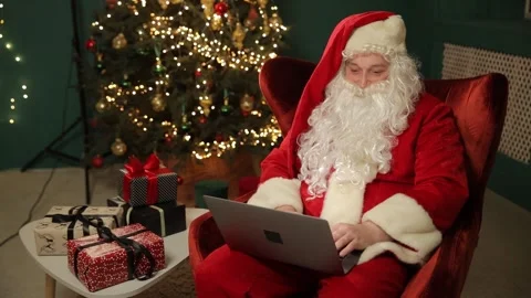 Santa Claus in a comfortable chair, using a modern laptop, and in front of him Stock-Footage 318291096