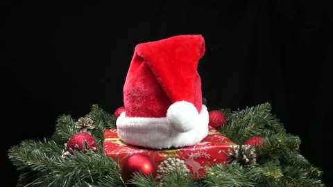 Santa Claus hat on a gift surrounded by green Christmas tree branches Stock Footage 159187166
