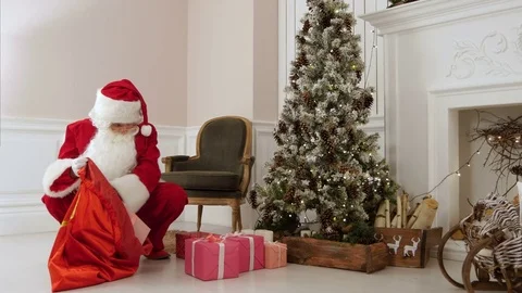Santa Claus putting presents back into his bag by Christmas tree Video stock 70948903