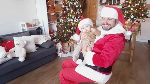 Santa Claus in a red and white outfit plays with a baby Stock Footage 165462706