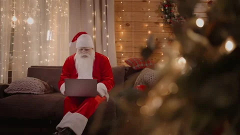 Santa Claus remote work from home sitting on the couch with a laptop near the Stock Footage 166392947