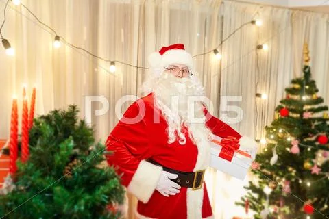 Santa Claus in a room decorated with a gift in hand on Christmas before the N Stock Photos