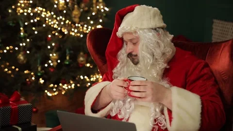 Santa Claus is shown multitasking with tech while enjoying coffee Stock Footage 318294587