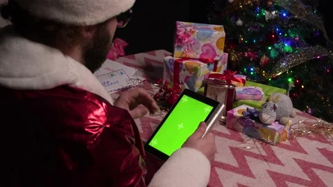 Santa Claus sits at a table with a tablet in his hands and flips through web Stock Footage 144848945
