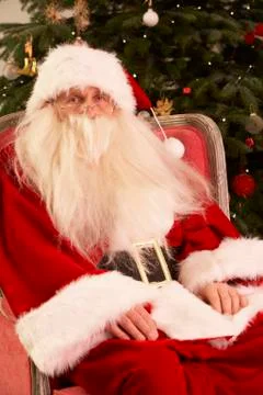 Santa Claus Sitting In Armchair In Front Of Christmas Tree Stock Photos