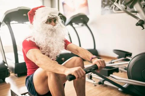 Santa claus training in rowing machine after christmas holidays reducing his  Foto stock