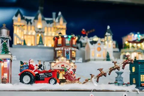 Santa drives a tractor pulling a sleigh through a festive holiday village scene Stock Photos