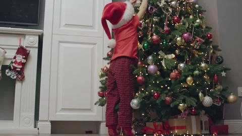 Santa hat-clad boy decorates Christmas tree festive cheer magic and excitement Stock Footage 285794289
