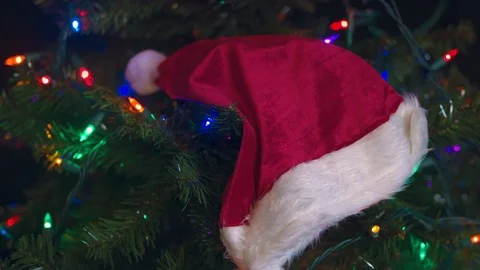 Santa Hat Hanging on a Tree Illuminated by Christmas Lights Stock Footage 98961180