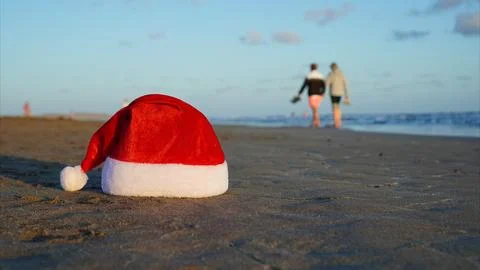Santa hat resting on beach sand with people walking Stock Photos