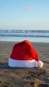 Santa hat resting on sandy beach by ocean Stock Photos