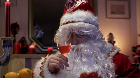 Santa pours and drinks a drink sitting at the Christmas table. Stock Footage 169028933