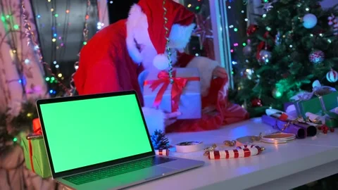 Santa putting wrapped gift box into sack near laptop with green screen Stock Footage 288278601