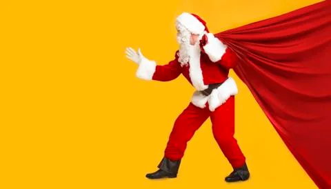 Santa trying to pull big bag with Christmas gifts on orange Stock Photos