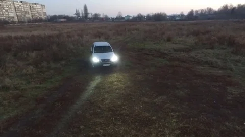 Сar rides on the field at dusk with headlights on. Aerial view Stock Footage 70645158